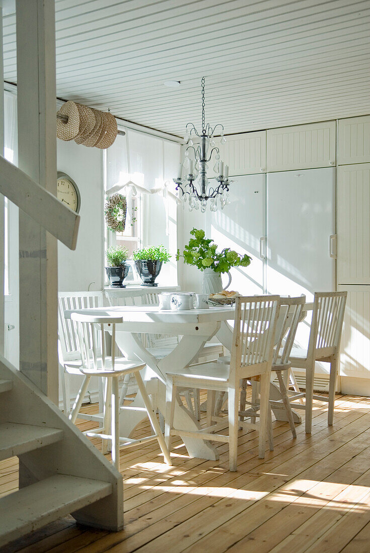 White dining area with wooden table, chairs and chandelier next to a wooden staircase