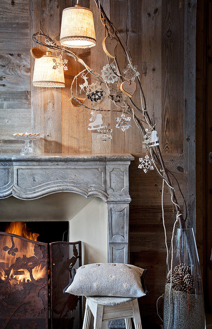 Christmas decorations on twigs in front of open fire and wood-panelled wall