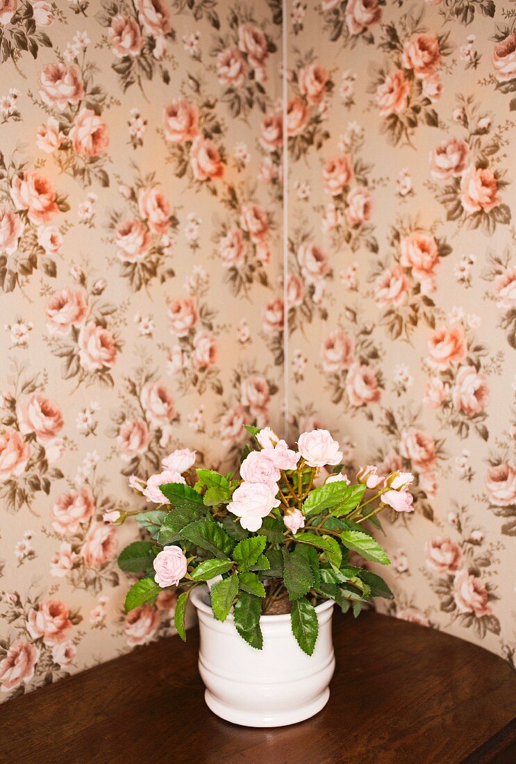 Flowerpot with plastic plant on table against floral wallpaper