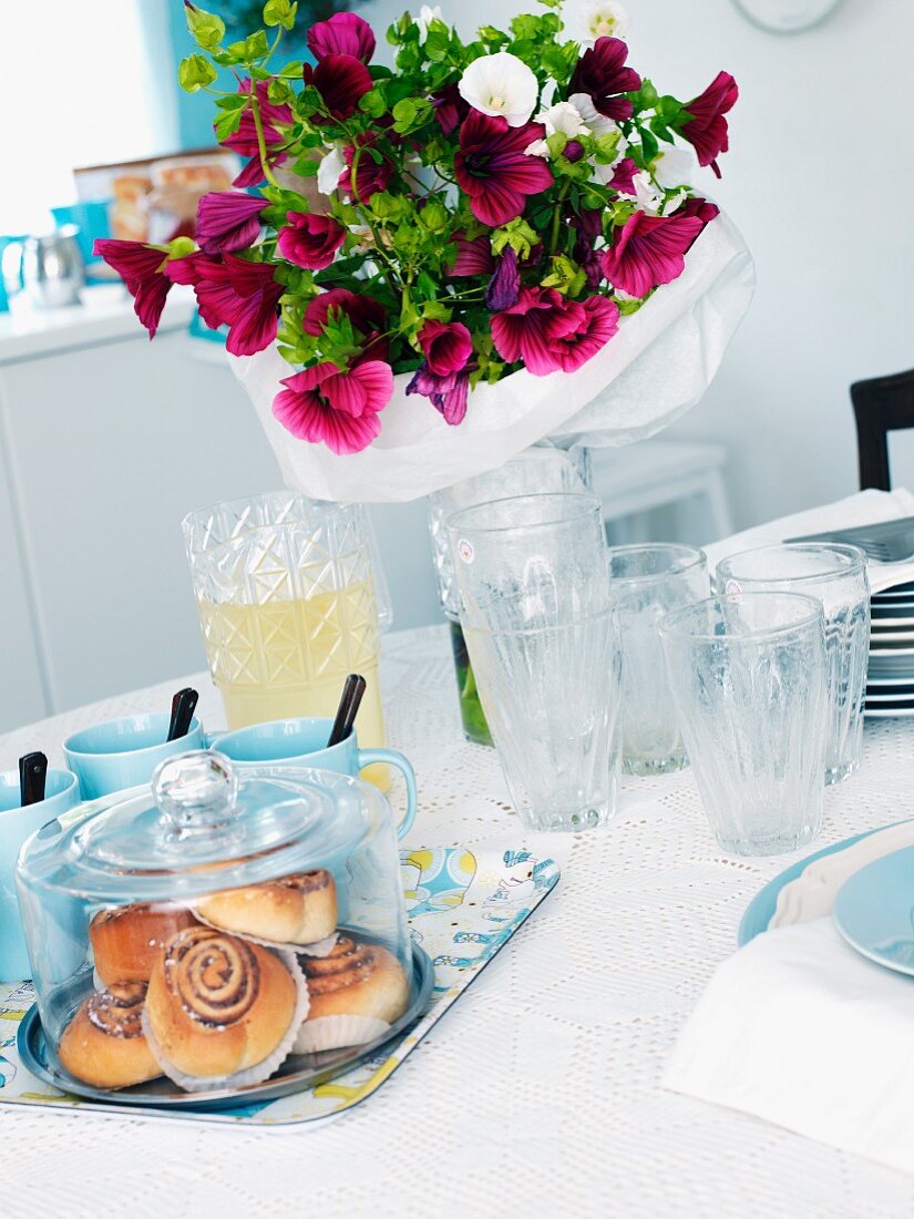 Zimtbrötchen unter Glashaube und sommerlicher Blumenstrauss auf einem Tisch