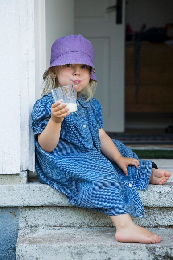 Mädchen sitzt mit einem Glas Milch im Hauseingang