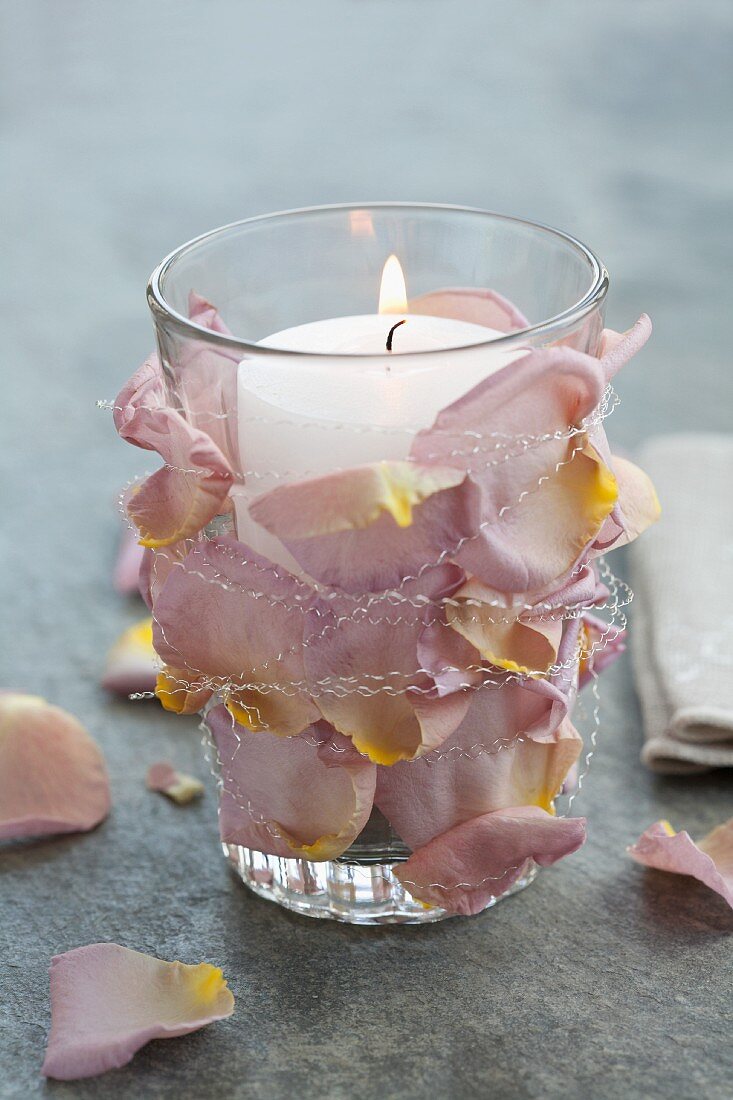 Glas mit Rosenblütenblättern und Kerze