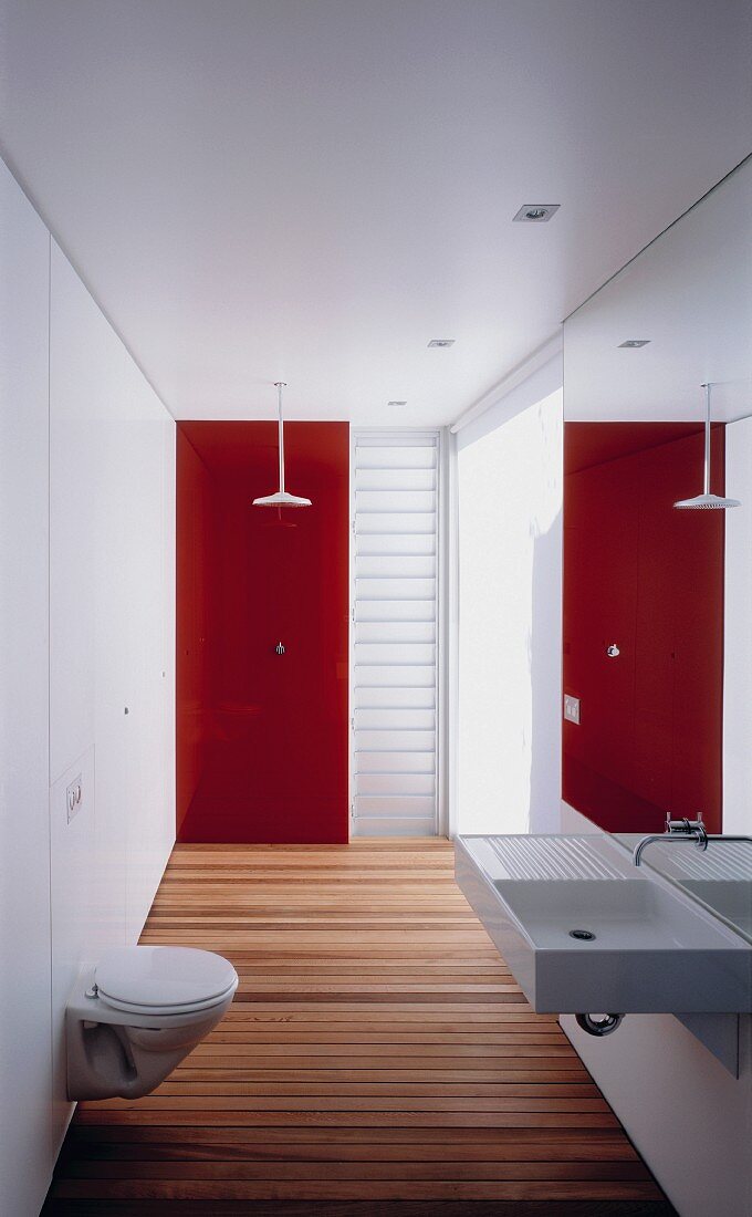 Schmales Designerbad mit Holzdielen und roter Glaswand