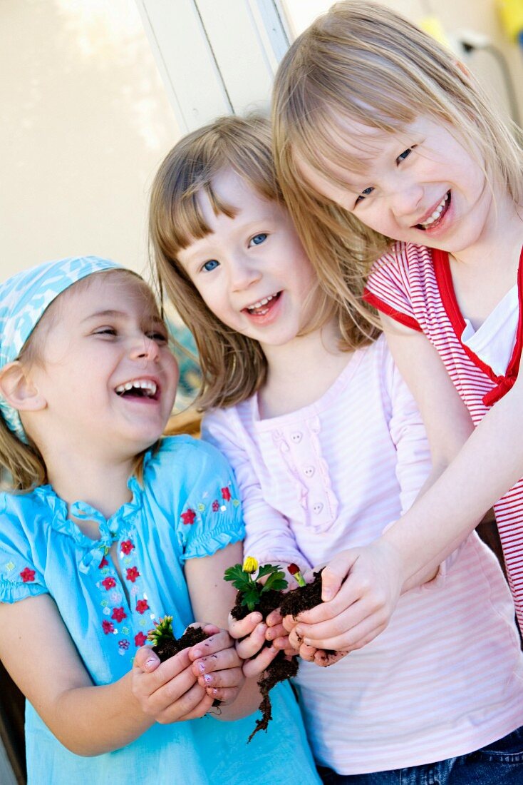 Drei Mädchen halten Blume mit Erdballen in den Händen