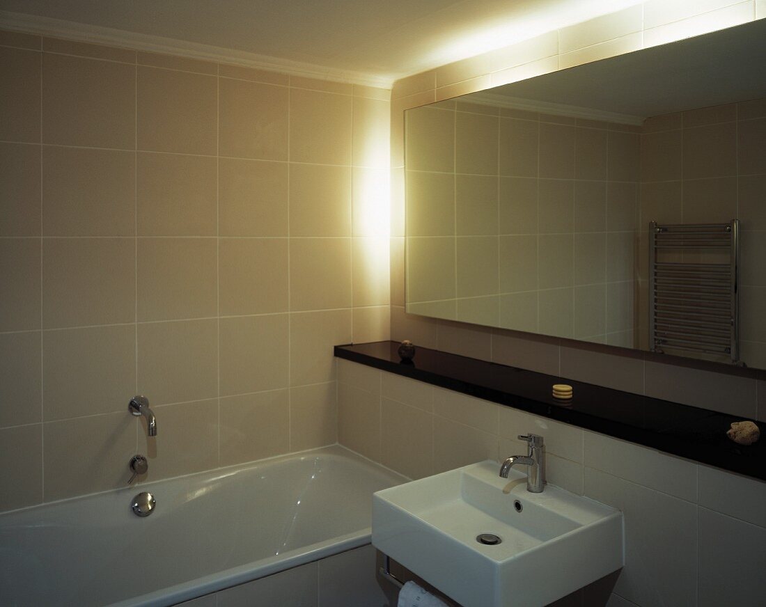 Corner of minimalist bathroom with back-lit mirror