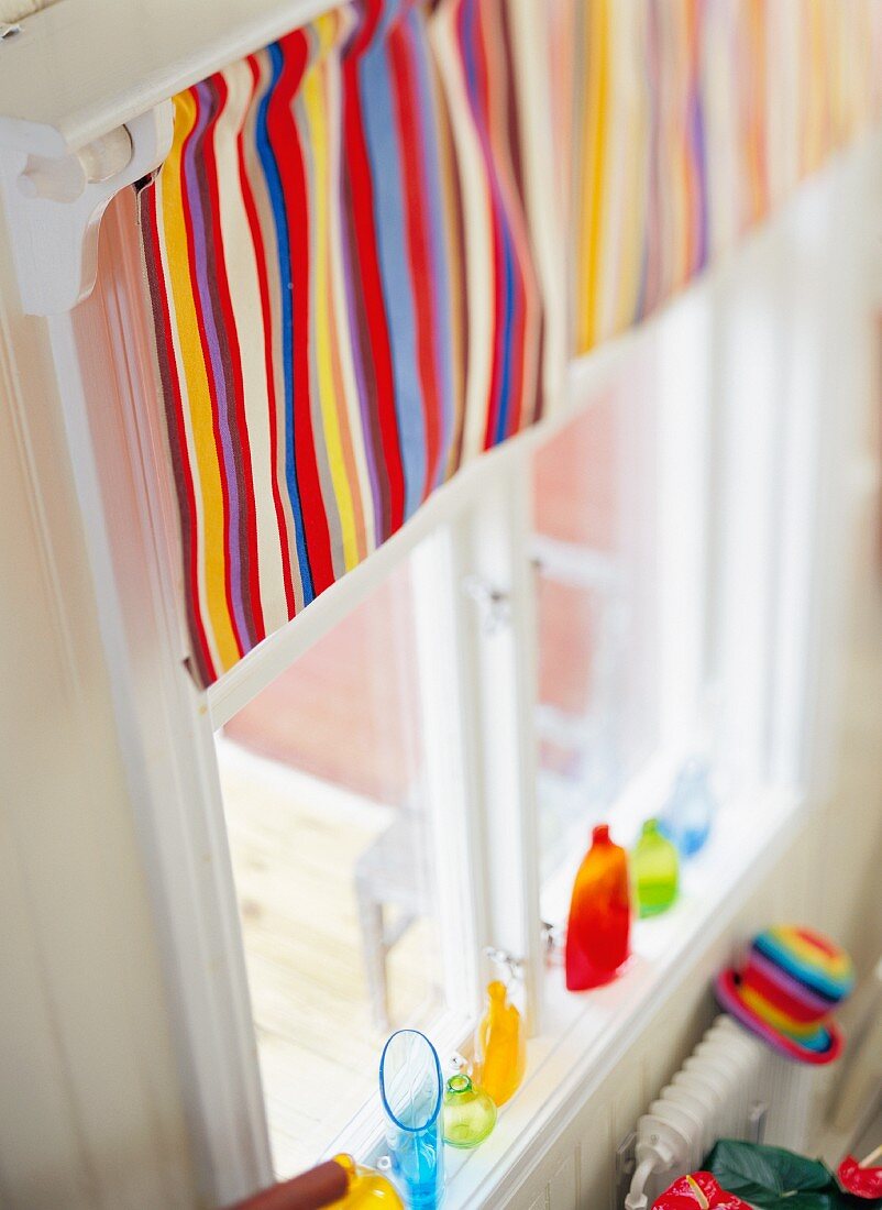 Bunt gestreifter Vorhang am Fenster, bunte Vasen auf der Fensterbank