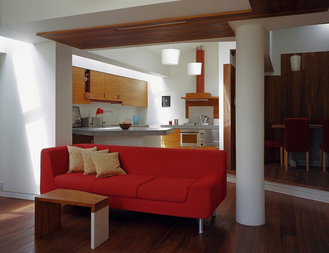 Beistelltisch vor rotem Sofa im Durchgang mit Blick auf offene Küche
