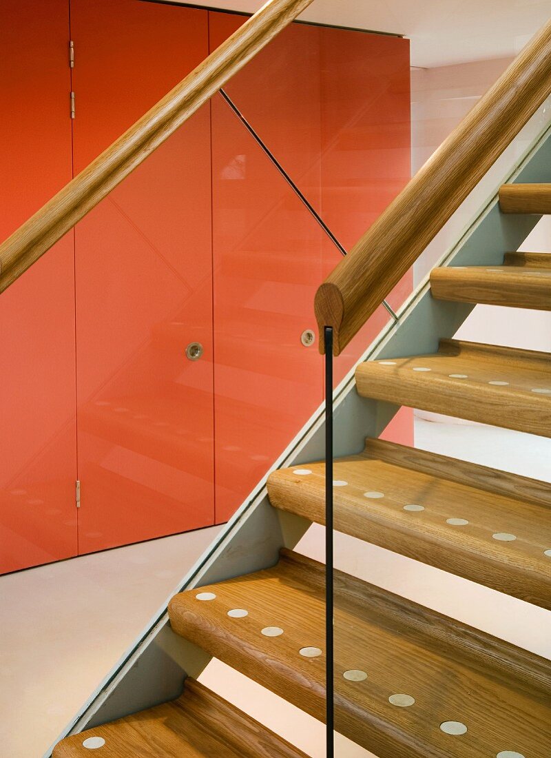 Staircase with wooden treads and view of fitted cupboards with red doors through glass balustrade
