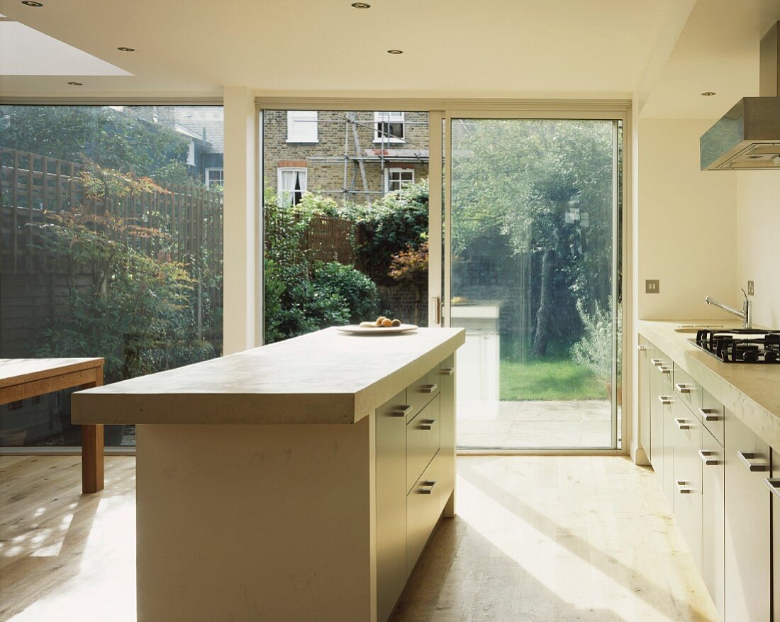 Eine helle Küche mit Kücheninsel und Glasfront zu der Terrasse