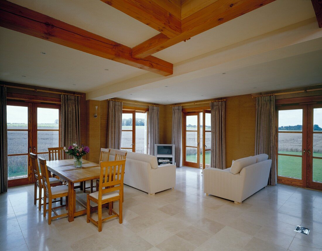 Kühle Steinplatten im offenen Wohnraum eines Holzhauses mit schlichter Möblierung und rundum Fenstertüren