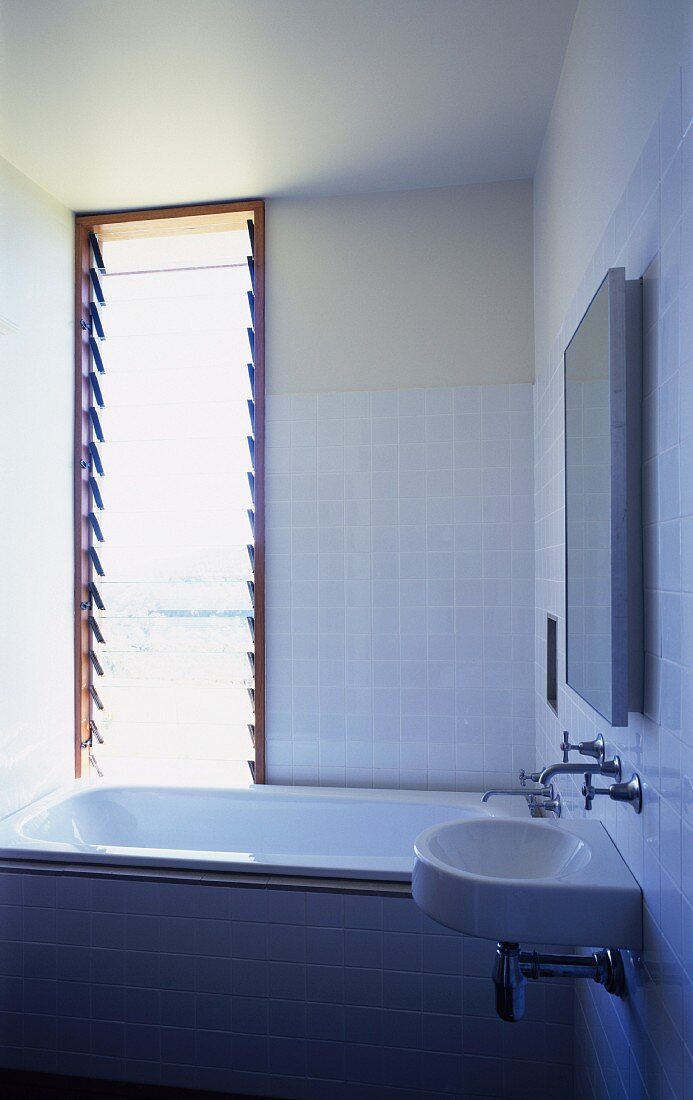 Moderne weiss geflieste Badezimmerecke mit Badewanne vor Fenster mit gekippten Glaslamellen