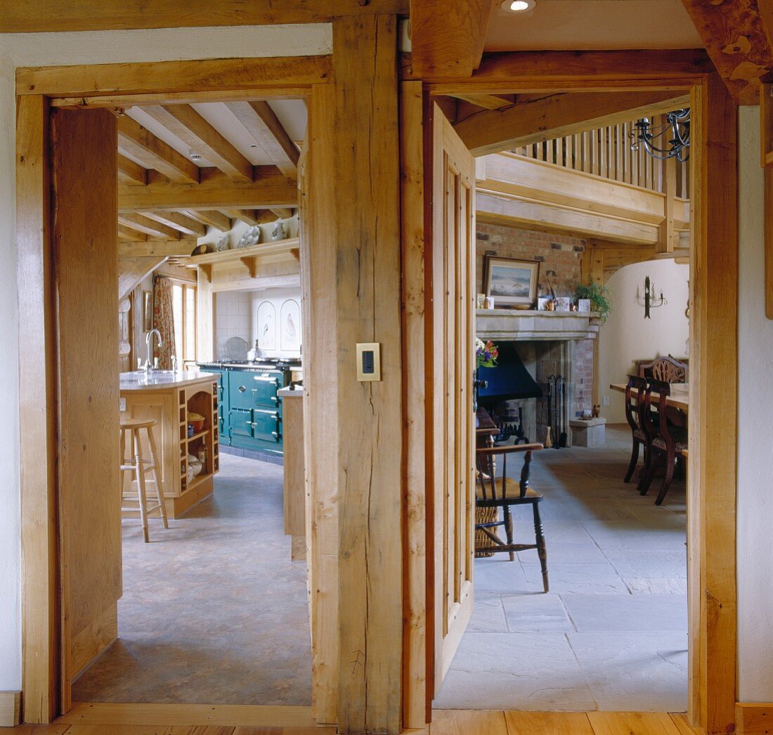 Blick durch nebeneinanderliegende Holztüren in Landhausküche und rustikales Esszimmer mit Kamin
