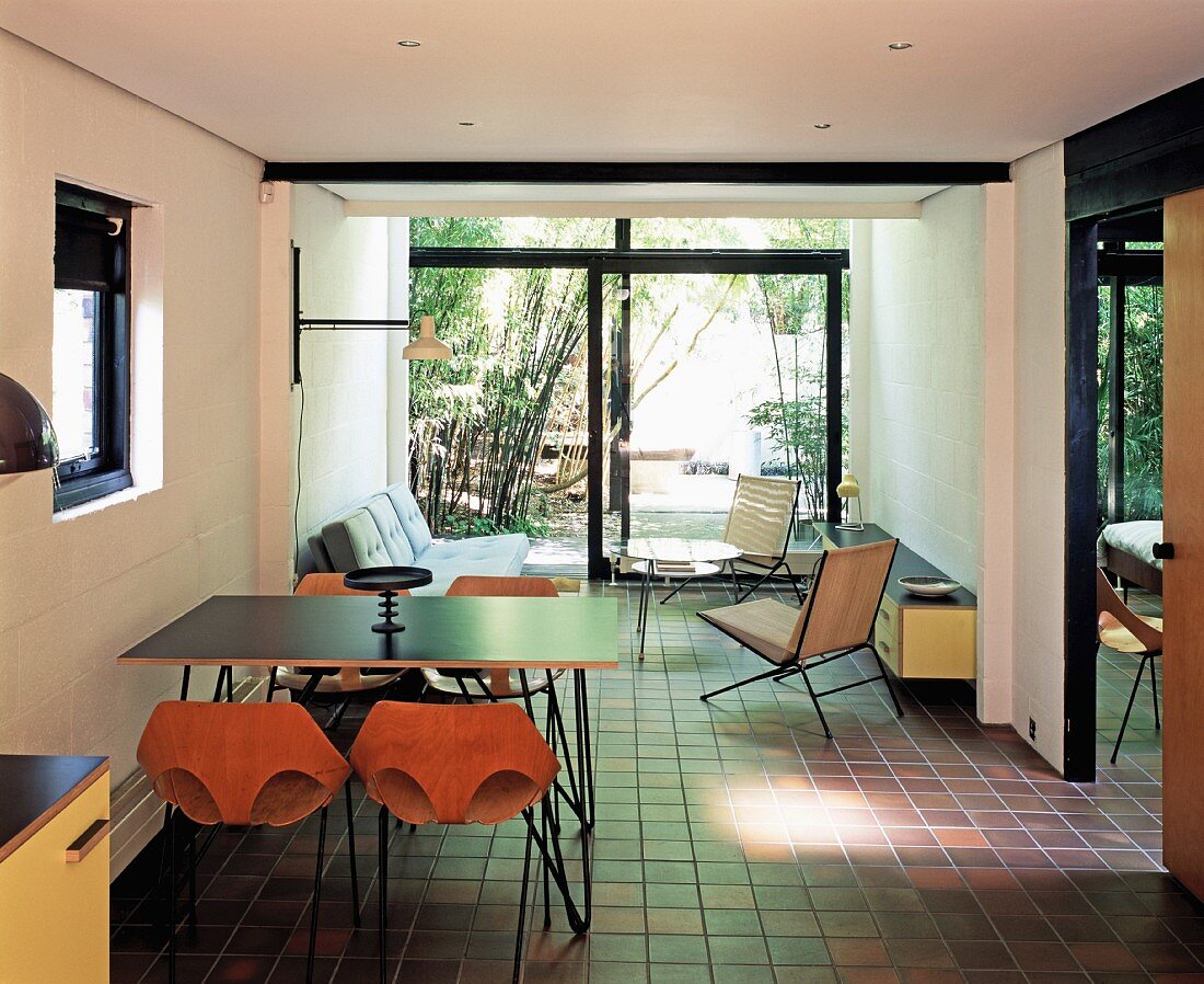 A modern living room with 1950s-style furniture, brown tiles and view into a bamboo garden