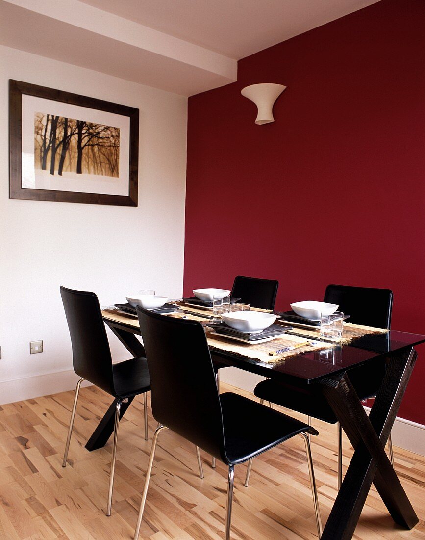 Set dining table with black chairs in front of dark red wall