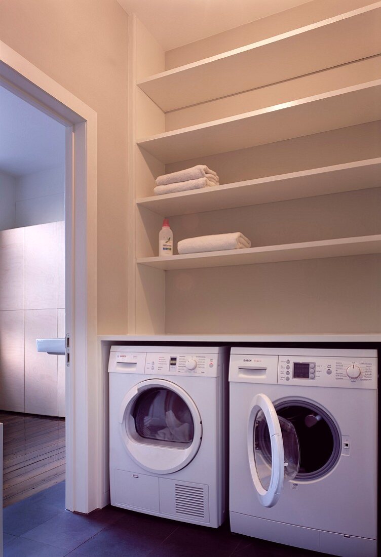 Utility room with two washing machines below shelving