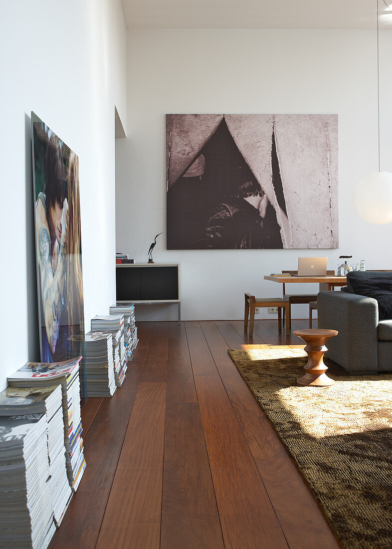 Wohnraum mit modernen Bildern an der Wand und Zeitschriftenstapel auf dunklem Dielenboden