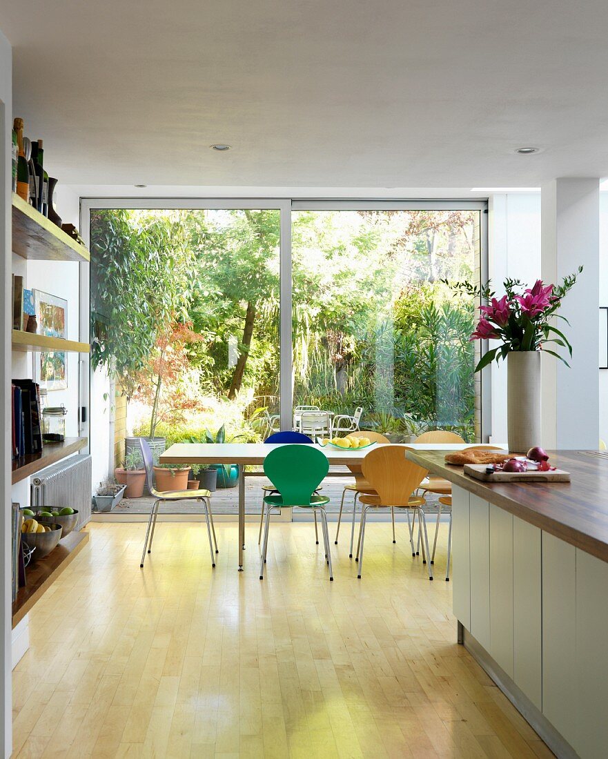 Farbige Schalenstühle aus Bauhauszeit am Esstisch vor raumhoher Fensterfront mit Gartenblick