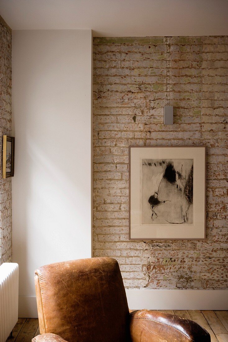 Exposed brick wall in corner of living room and part of a leather armchair