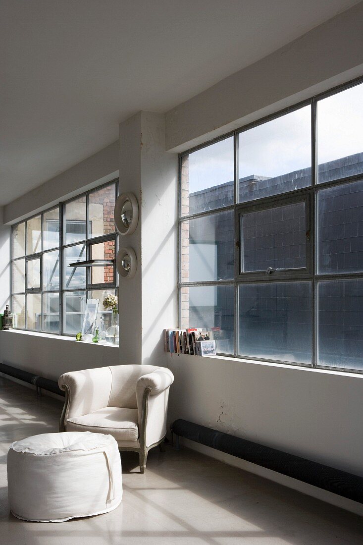 Barocker Sessel und moderner Sitzhocker vor Industriefenster im Loft
