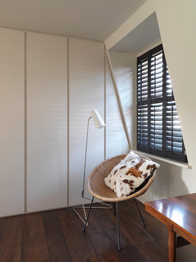 Circular, rattan shell chair with cushion below window with closed shutters
