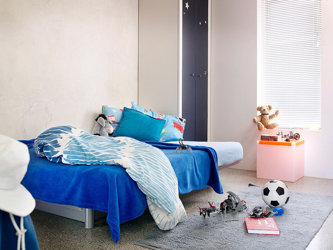 Bett mit blauer Decke und Spielzeug auf dem Boden in kleinem Kinderzimmer
