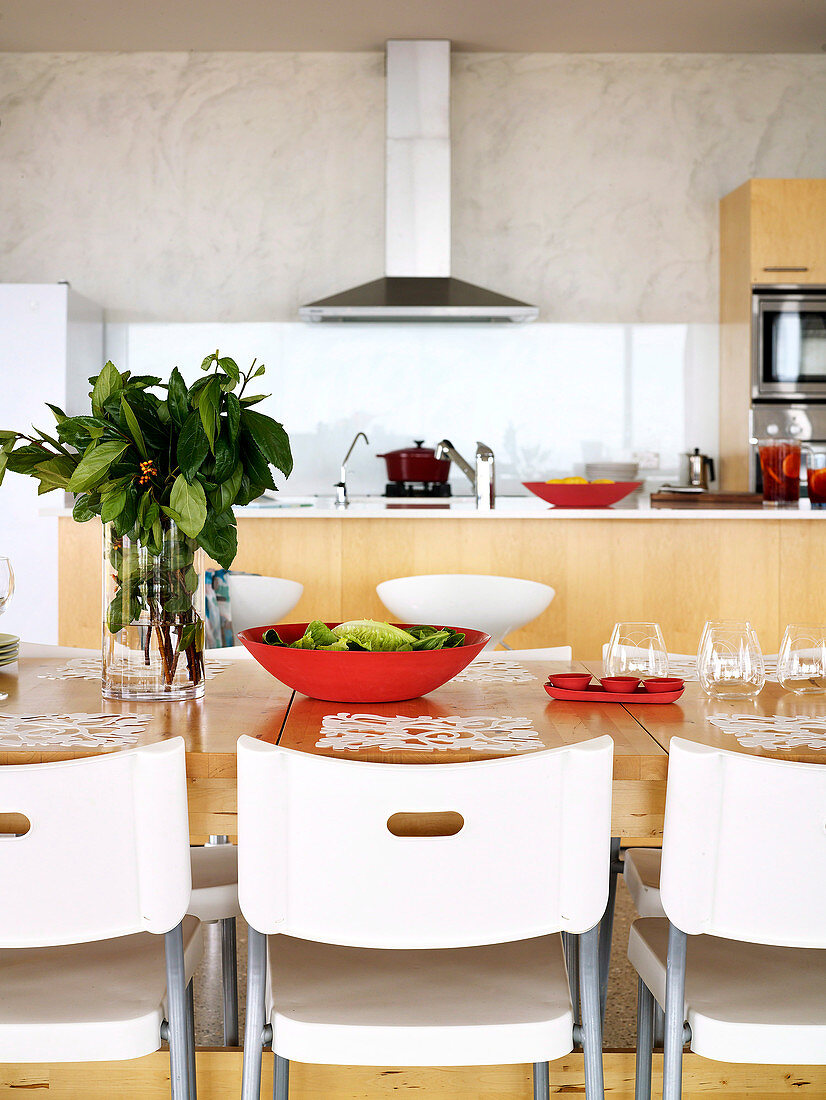 weiße, moderne Kunststoffstühle an einem gedeckten Holztisch in der offenen Küche