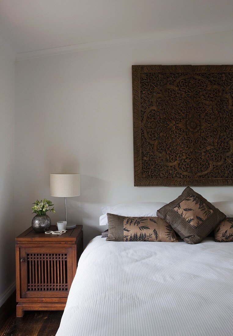 Simple bedroom with Oriental tapestry above bed and antique, wooden bedside table