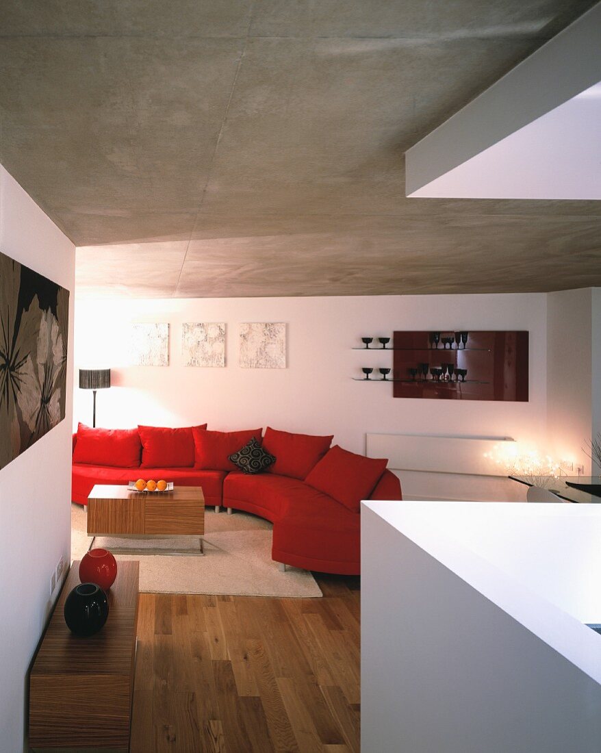 Living space with curved red couch below grey concrete ceiling