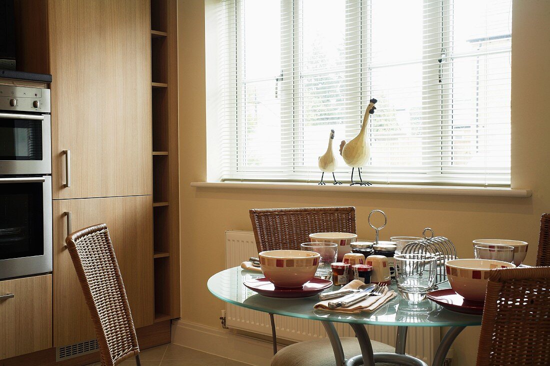 Table set for breakfast below window with half-closed blinds in kitchen