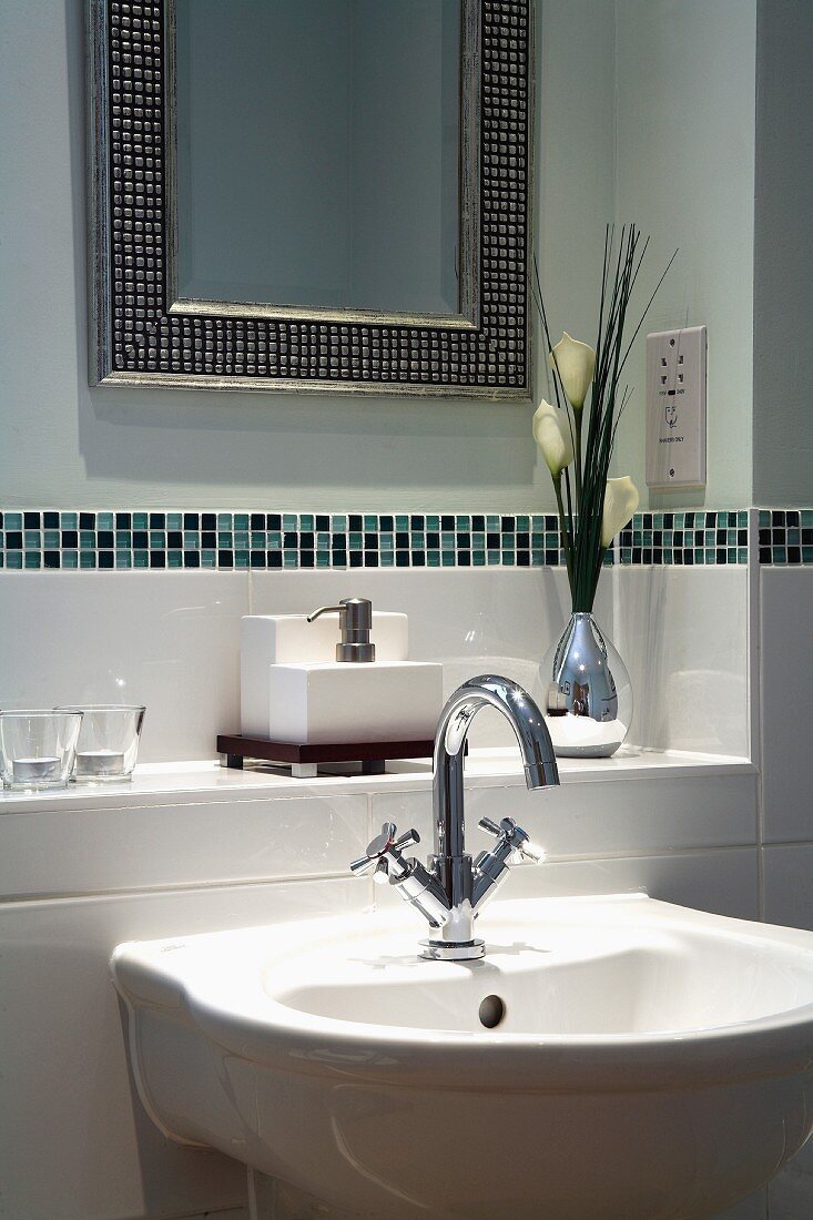 Waschbecken vor gefliester Ablage mit Bordüre und gerahmter Spiegel