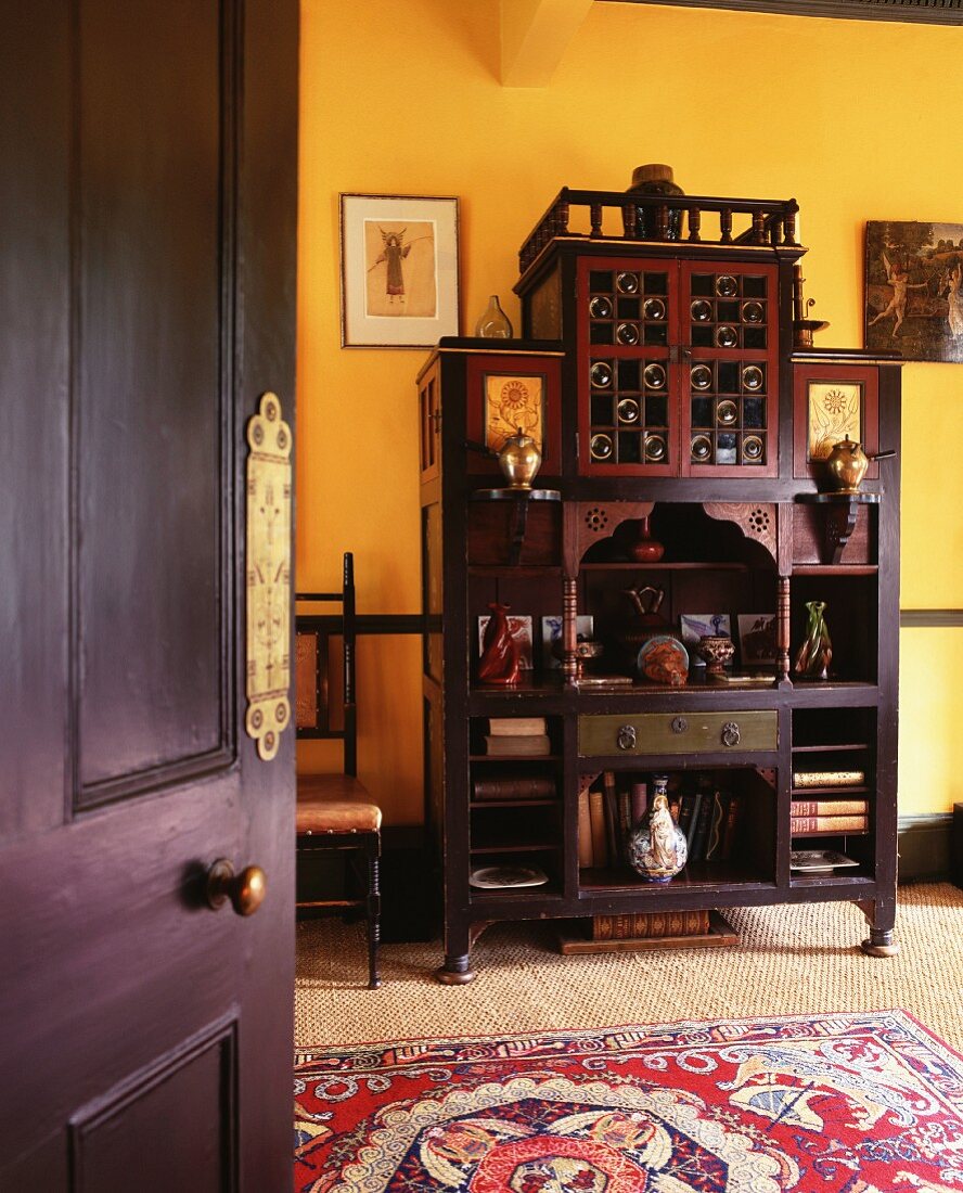 View of Oriental dark wood cupboard against yellow-painted wall through open door
