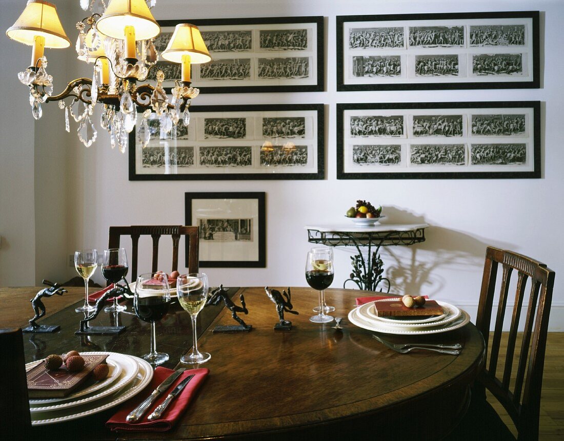 Place settings and filled wine glasses on wooden table in front of wall with framed pictures