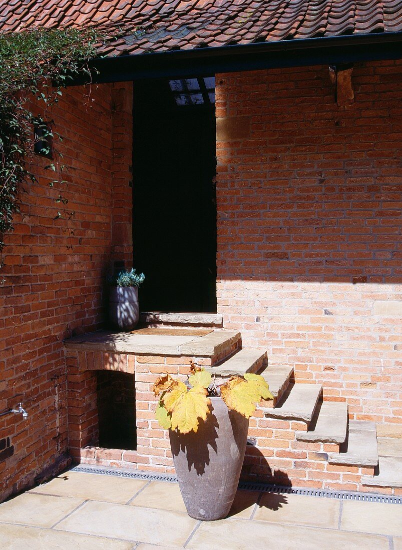 Haus und Eingangstreppe aus Ziegel und Tongefäss mit Blättern in Herbstfärbung