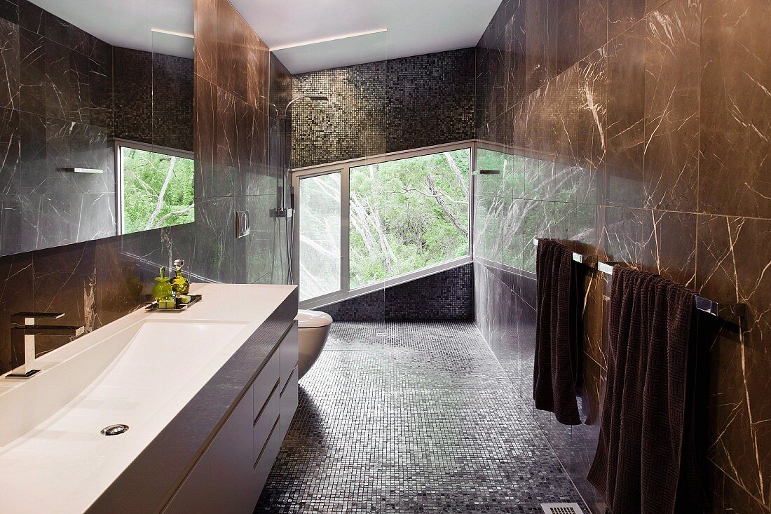 Elegantes Designer Bad mit braun marmorierten Steinfliesen an Wand und grosszügigem Waschtisch