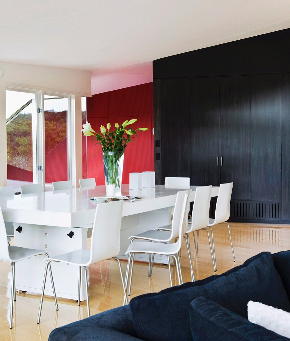 White designer dining table and chairs in front of black fitted cupboard in modern living-dining room