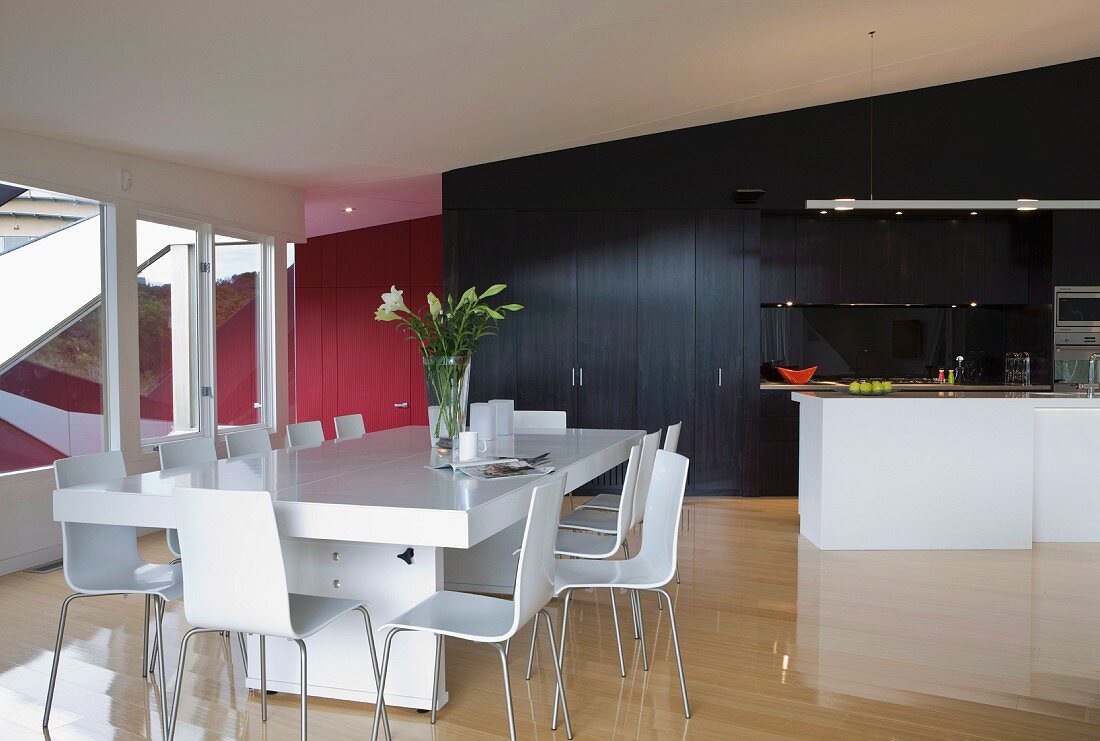 Moderner Esstisch und Stühle in Weiß vor freistehender Küchentheke und schwarzem Einbauschrank in offenem Wohnraum