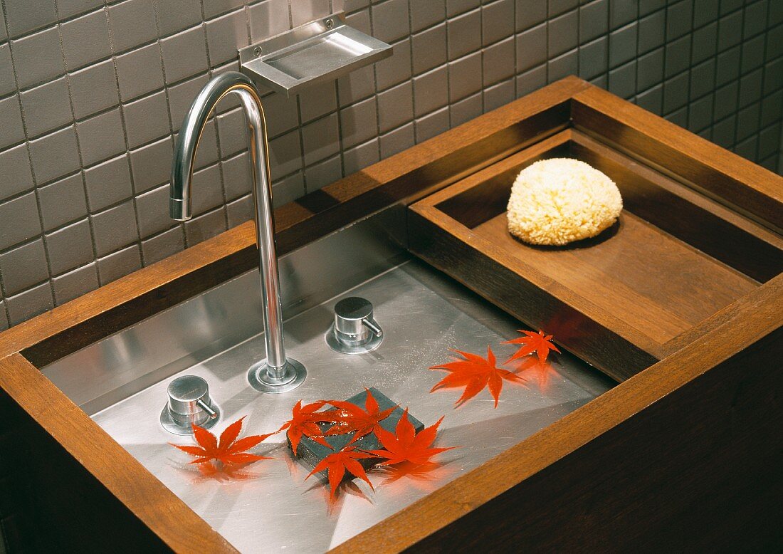 Blätter mit roter Herbstfärbung liegen im minimalistischen Designer Waschtisch aus Holz und Edelstahl