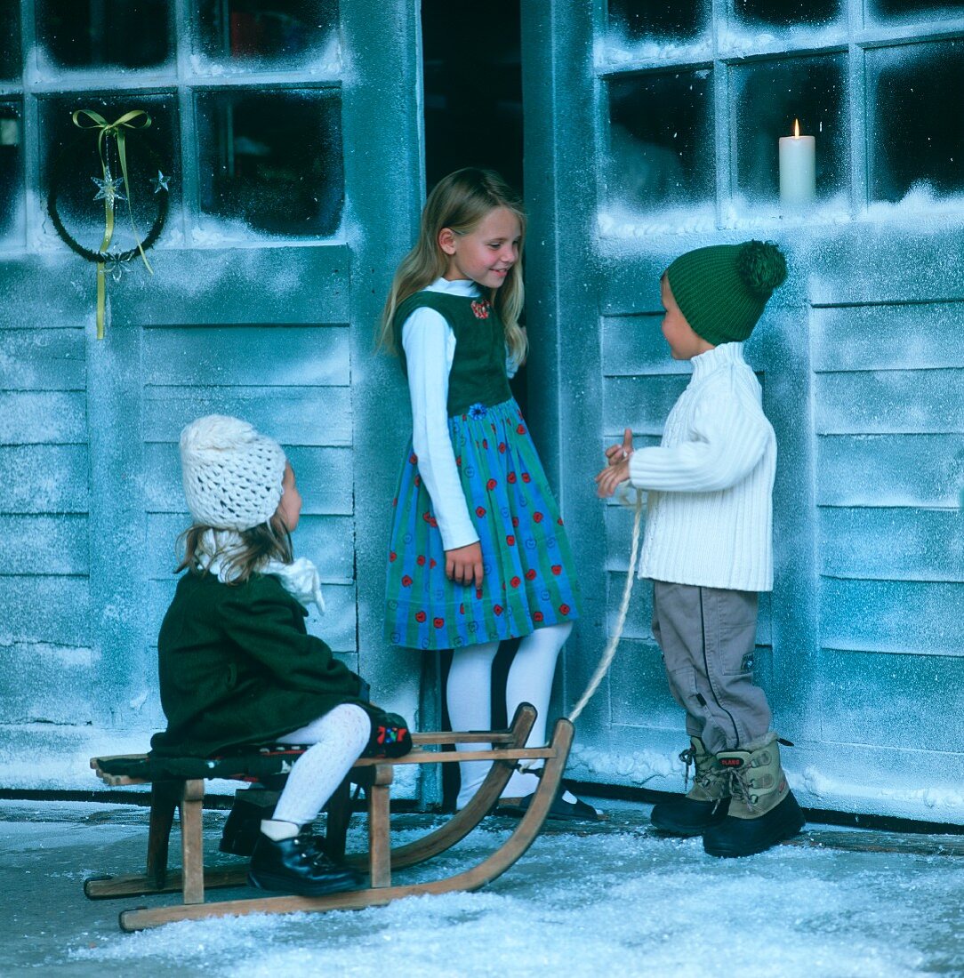 Drei Kinder mit Schlitten vor dem Haus