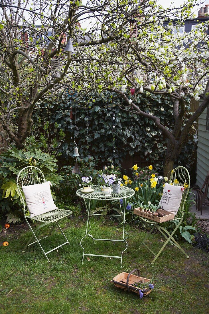 Gartentisch mit zwei Gartenstühlen unter einem österlich dekoriertem Baum