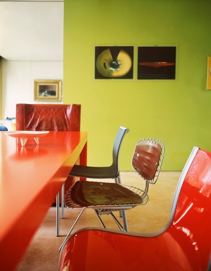 Roter Tisch aus Kunststoff mit Stühlen im Stilmix vor grün getönter Wand