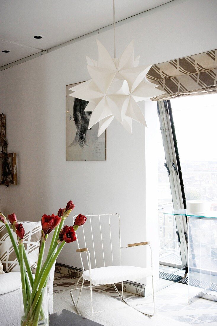 Paper star lightshade and old, white-painted metal rocking chair in front of slanting panoramic window