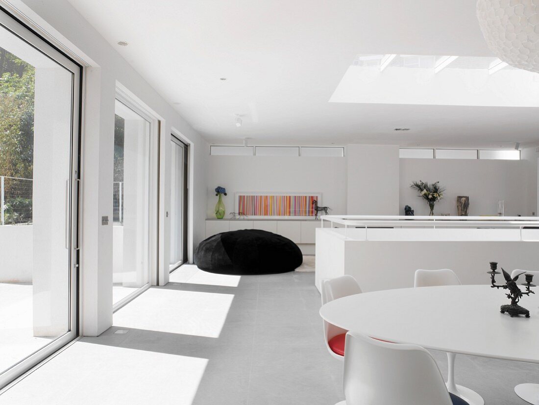 Essplatz mit Design-Klassikern und voluminöser Sitzsack im weissen, sonnigen Wohnraum mit Oberlicht und breiten Schiebetürfronten