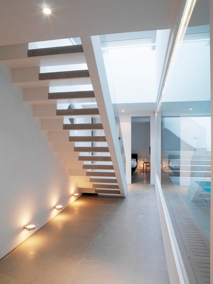 Mit Wandstrahlern beleuchtete Treppenuntersicht neben Glasabtrennung zum Haus-Pool