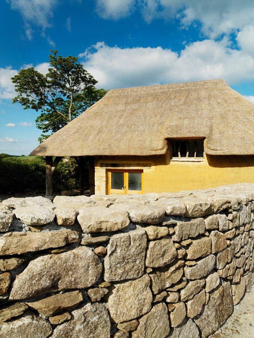Clay house with thatched roof behind stone wall