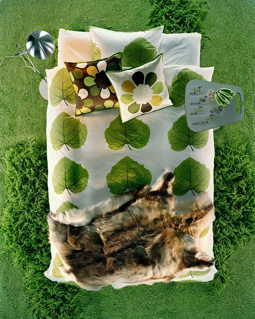 Moderne, grüne Oase mit Tierfell auf Bettwäsche im Pflanzenmuster