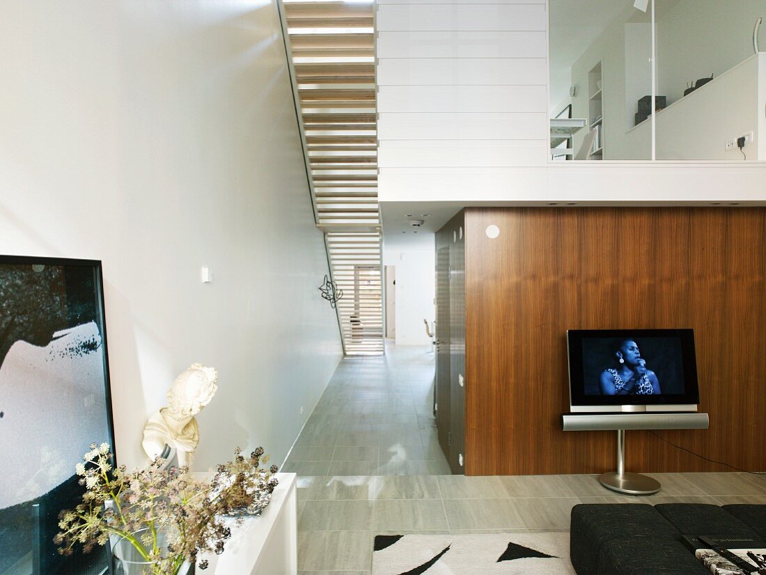 Double-height living room, view of stairs from below and glazed gallery level in modern house with narrow floor plan