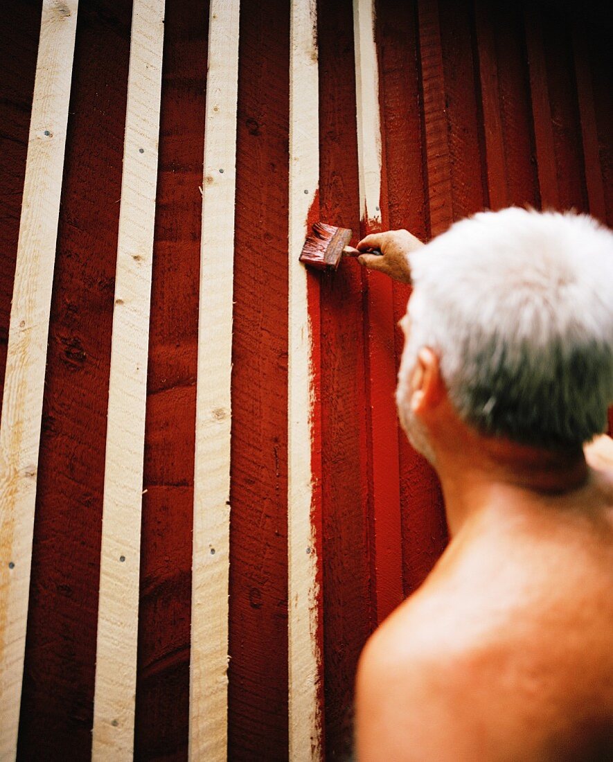 Mann streicht Holzfassade eines Hauses