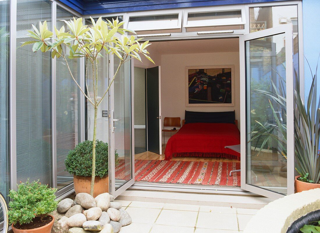 Kleine Innenhof-Terrasse im zeitgenössischen Stil und Blick auf Doppelbett mit knallroter Tagesdecke