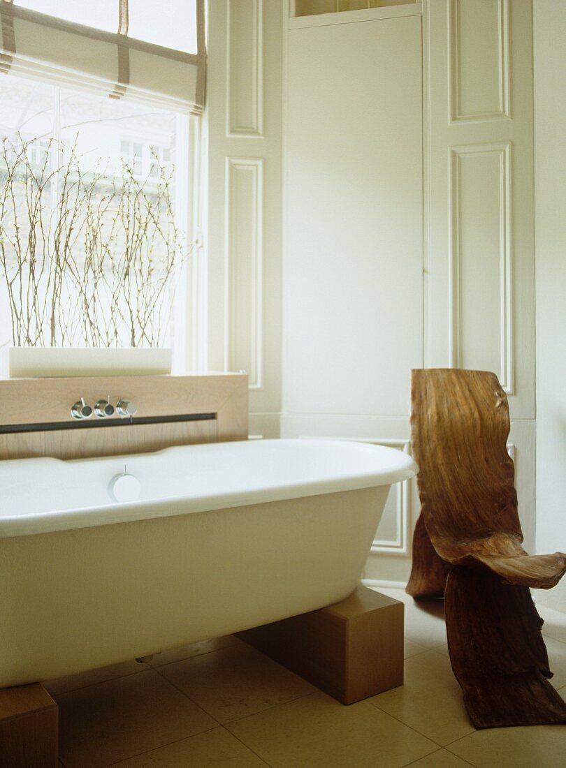 Freistehende moderne Badewanne auf Holzblöcken und organisch geformter Stuhl aus Schälholz