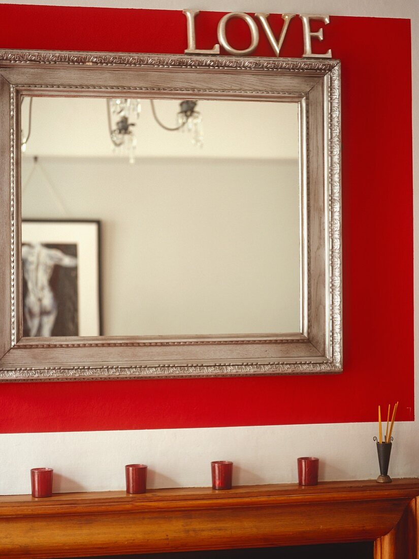 Love-Spiegel mit silbernem Holzrahmen auf roter Wand und Spiegelung eines männlichen Aktes